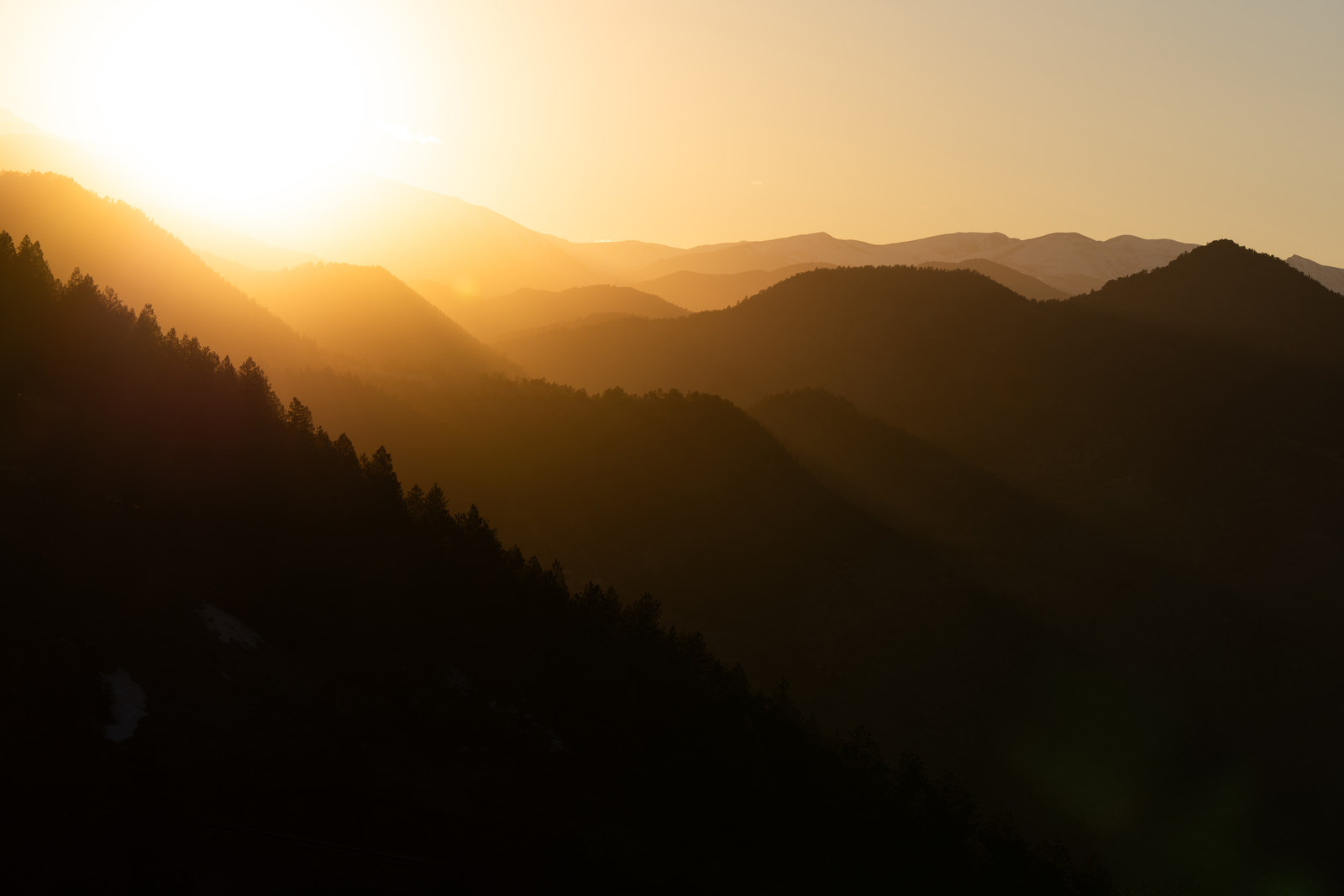 Layered forested ridges fading into golden haze as the sun sets over the foothills above Golden, Colorado