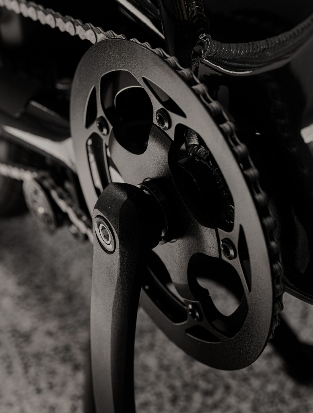 Close-up of an e-bike's black chainring, crank arm and chain, in muted sepia tones